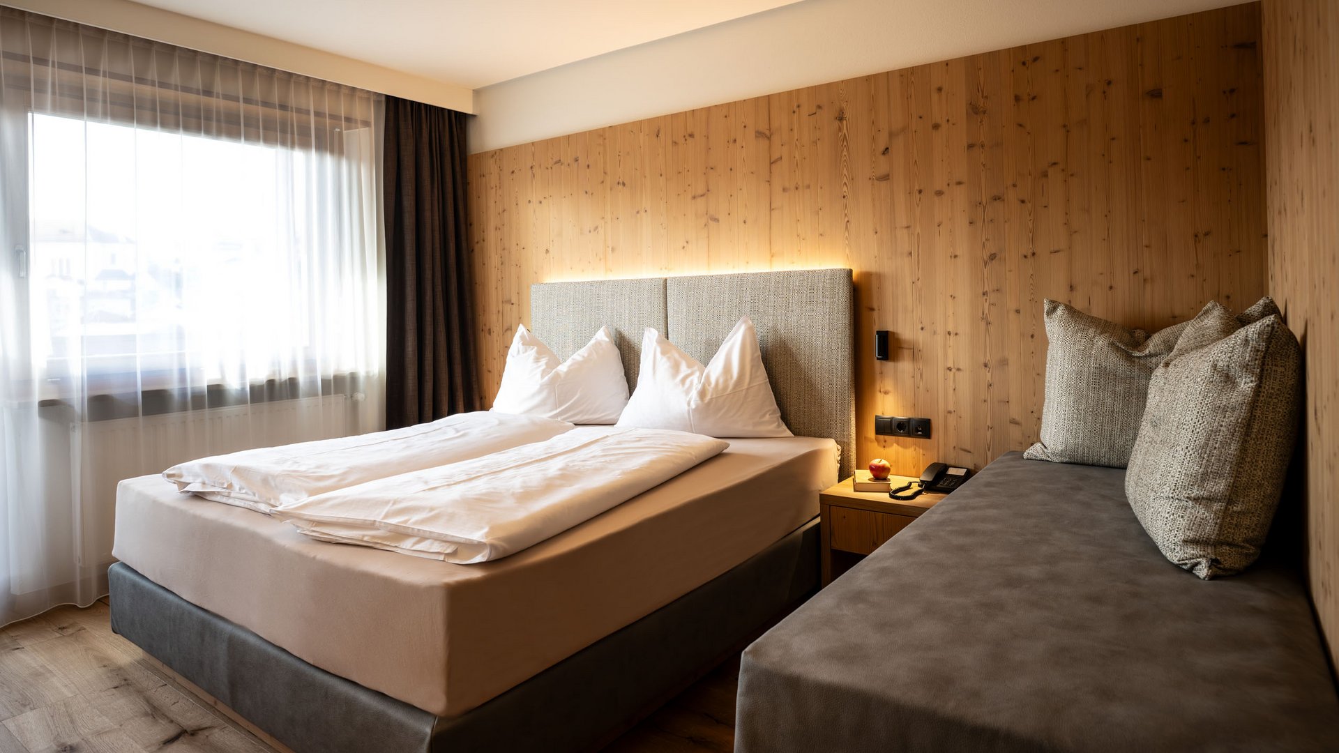 Urlaubsglück in der Unterkunft in Kastelruth Gemütliches Hotelzimmer mit Doppelbett und Sitzbank vor Holzverkleidung